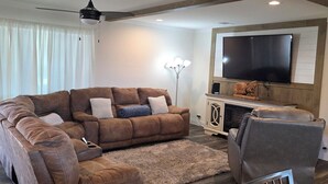 Un salon moderne avec un canapé d’angle, un fauteuil gris et un téléviseur fixé au mur.