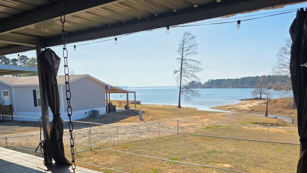 Une véranda abritée avec une balançoire, une vue sur un lac et une maison en arrière-plan.