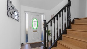 A staircase with wooden steps and black balusters, a white door with a green glass window, and a wall-mounted mirror.