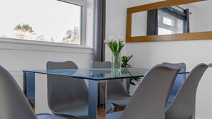 A modern dining area with a glass table, grey chairs, and a vase of flowers.