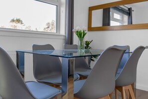 Un espace repas moderne avec une table en verre, des chaises grises et un vase rempli de fleurs.