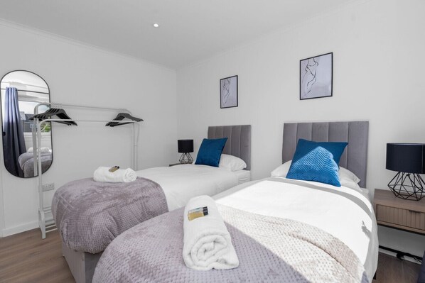 Habitación de hotel con dos camas, un espejo, un televisor montado en la pared y una mesita de noche pequeña con una lámpara.