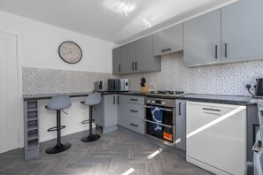 Une cuisine moderne avec des meubles gris, un four à micro-ondes, une cuisinière et deux tabourets de bar.
