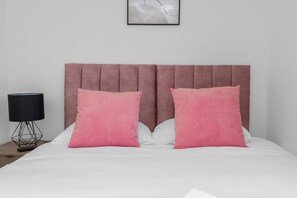 Un lit avec une tête de lit, deux oreillers, une table de chevet et une lampe.