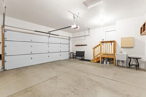 Un garaje con una puerta grande de color blanco, una escalera de madera, un banco y una mesa pequeña.