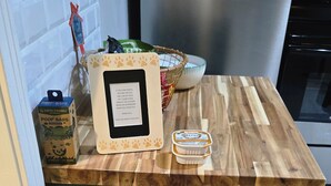 Una encimera de cocina con un refrigerador de acero inoxidable, un microondas y un bote de basura. Hay dos boles de metal sobre un tapete debajo de la encimera.