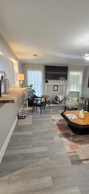A living room with a fireplace, a flat-screen TV mounted above it, a dining table with chairs, and a coffee table with candles and a book.