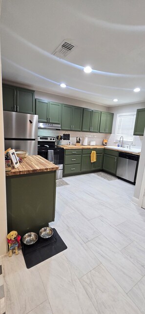 A modern kitchen with green cabinets, stainless steel appliances, and a wooden countertop.