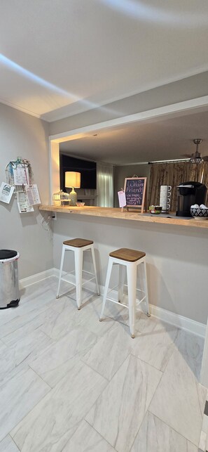 A modern kitchen with a bar area, two stools, a coffee machine, and a chalkboard sign.