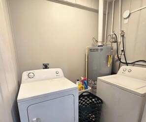 A laundry room with two washing machines, a water heater, and a laundry basket.