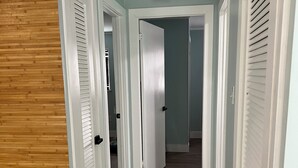 A hallway with wooden flooring, white doors with black handles, and a ceiling light fixture. - Delightful 2 bedroom - Island Cottage (Key Largo)