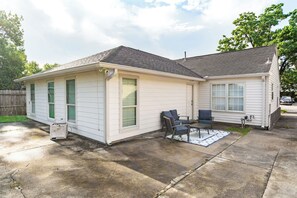 A single-story house with a garage, a patio with a table and chairs, and a small shed.