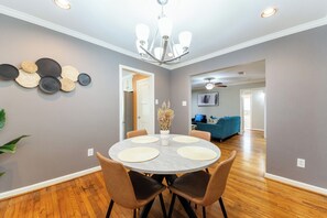 A dining area with a round table, four chairs, and a chandelier.