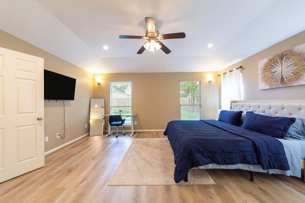 A bedroom with a bed, ceiling fan, and a desk with a chair.