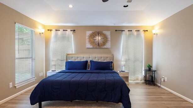 A bedroom with a large bed, a ceiling fan, and a decorative wall piece. - Culmore TX (Houston)