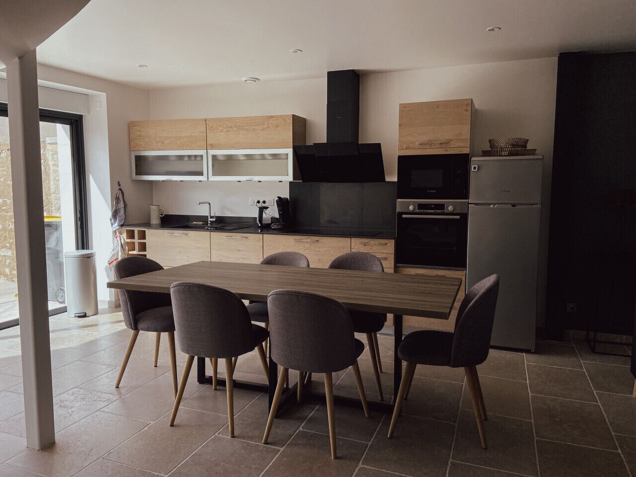 Eine moderne Küche mit Esstisch und Stühlen aus Holz, eingebauten Geräten und einem großen Fenster.