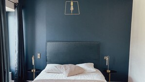 A bedroom with a bed, bedside tables, a bench, and a hanging light fixture.