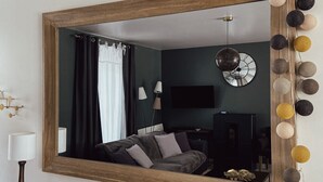 A modern living room with a large mirror, dark walls, a sofa, a lamp, and a clock.