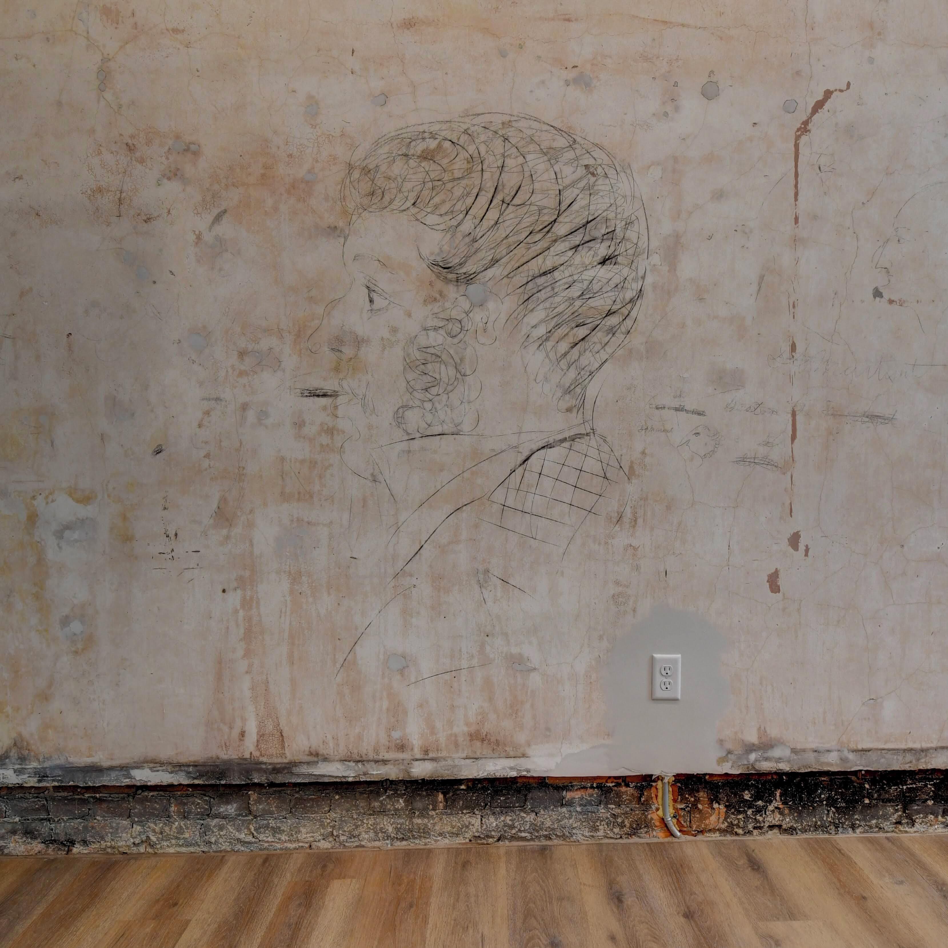 A wall with a faded sketch of a man's face and some writing.