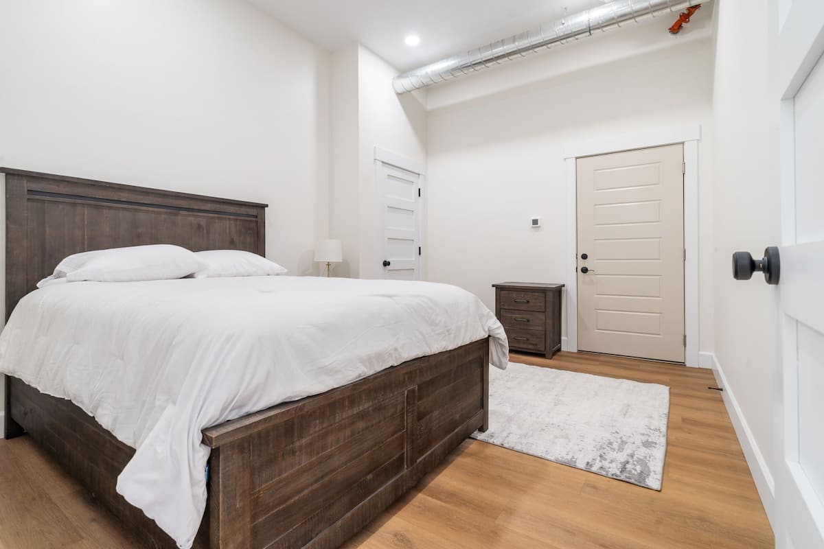 A bedroom with a wooden bed, a white rug, a nightstand, and a door.