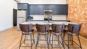 Una cocina moderna con armarios azul oscuro, salpicadero de azulejos blancos y pared decorativa de ladrillo.