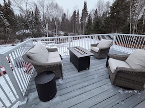 Une terrasse extérieure couverte, aménagée avec des meubles en osier et dotée d’un foyer.
