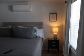 Une chambre d’hôtel avec un lit, une table de chevet avec une lampe, un climatiseur et une fenêtre avec des stores.