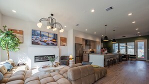 Una sala moderna con un amplio sofá modular, una chimenea y una cocina visible a través de un ventanal.