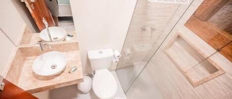 Un baño moderno con tocador de madera, un lavabo blanco, un inodoro y una cabina de ducha con paredes de vidrio.