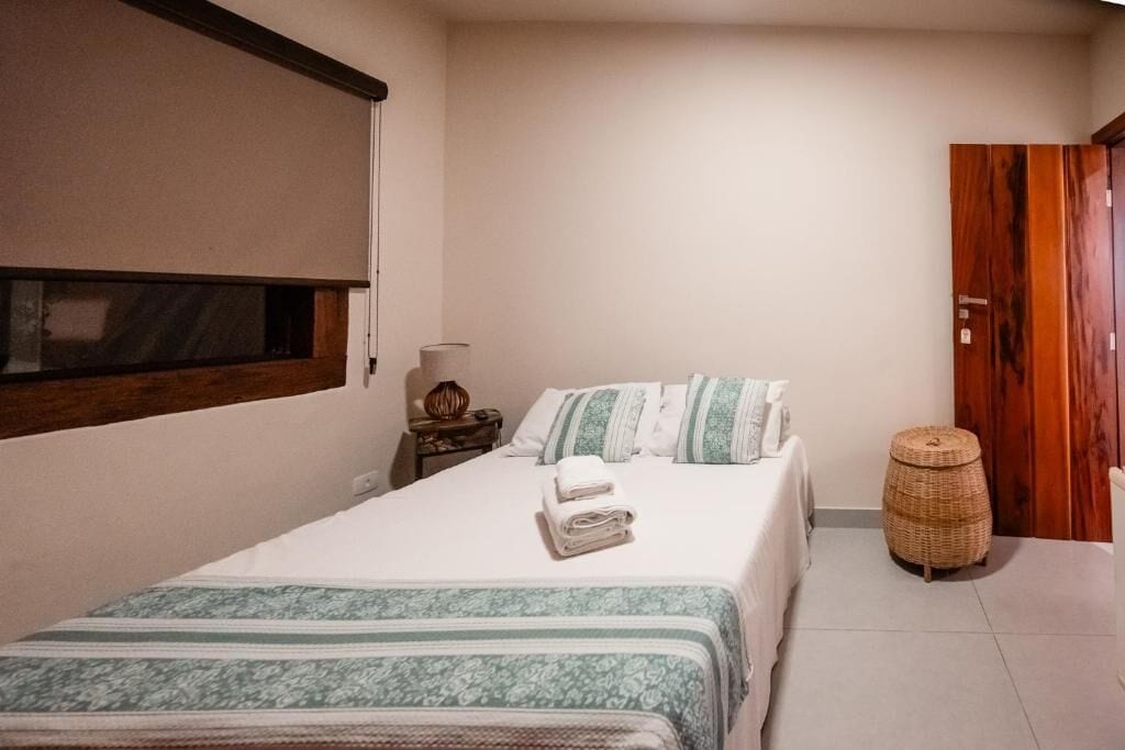 A bedroom with a bed, pillows, a bedside table, a lamp, and a wooden wardrobe.