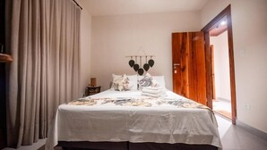 Een opgemaakt bed met een witte spreidek en decoratieve kussens, een houten deur en een wandlamp.