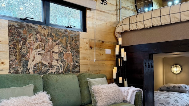 A cozy living room with a green sofa, a decorative tapestry, and a high ceiling with exposed beams. - Copper Castle & Petting Farm near Legoland (Windsor)