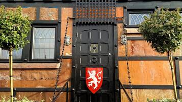 A medieval-themed building with a black gate, a knight statue, and a red shield emblem.