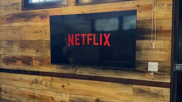 A wall-mounted television with the word "NETFLIX" in red letters, set against a wooden wall with two windows above it.
