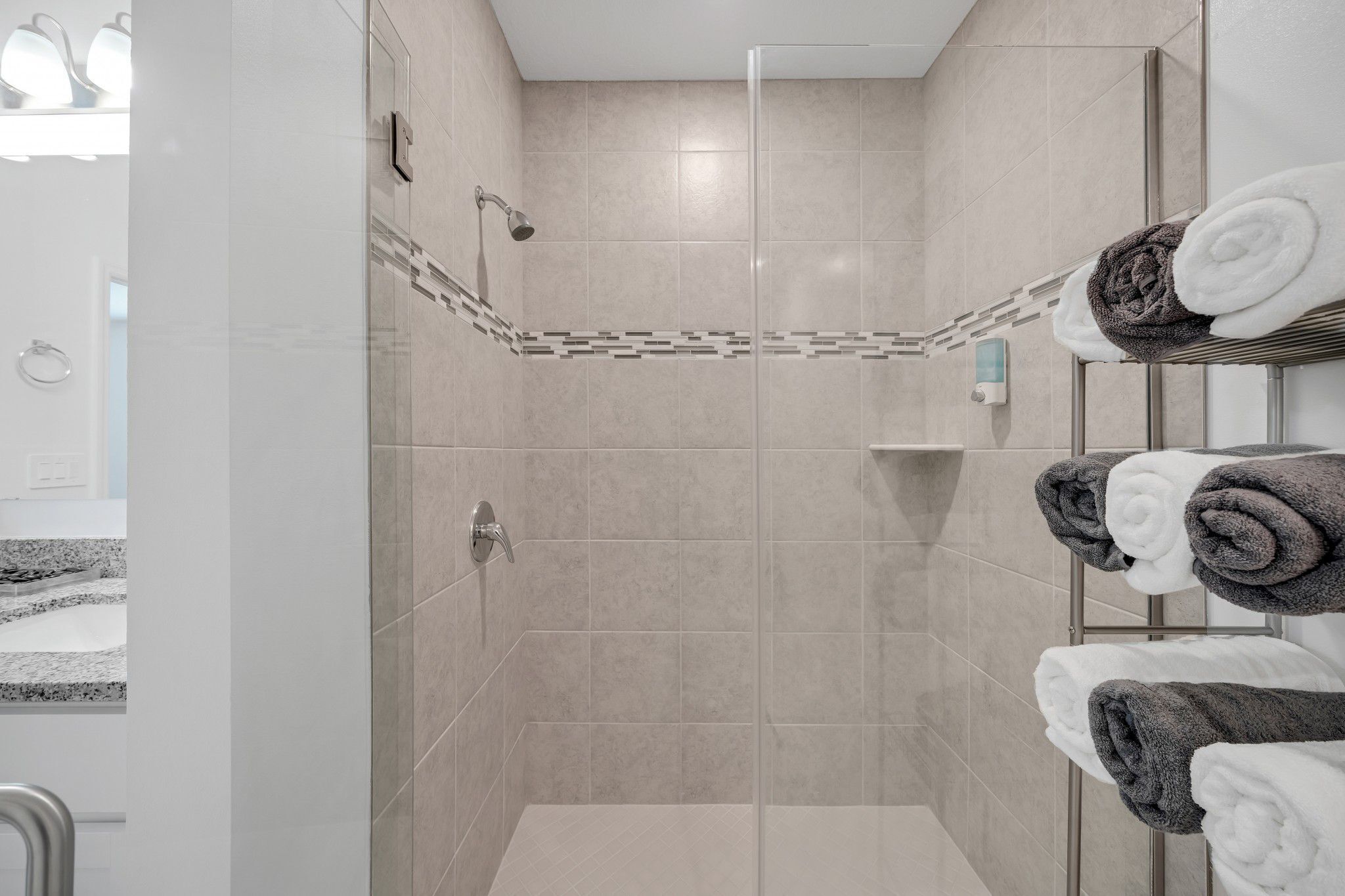 A modern shower area with beige tiles, a glass-enclosed shower, and a towel rack with neatly folded towels.