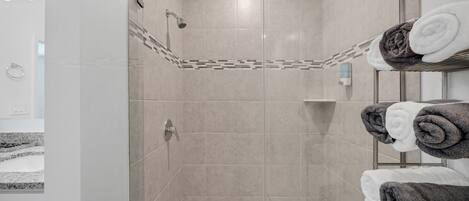 A modern shower area with beige tiles, a glass-enclosed shower, and a towel rack with neatly folded towels.