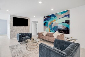Un salon moderne agrémenté d’un grand tableau abstrait, d’un téléviseur à écran plat et d’un canapé avec deux coussins décoratifs.