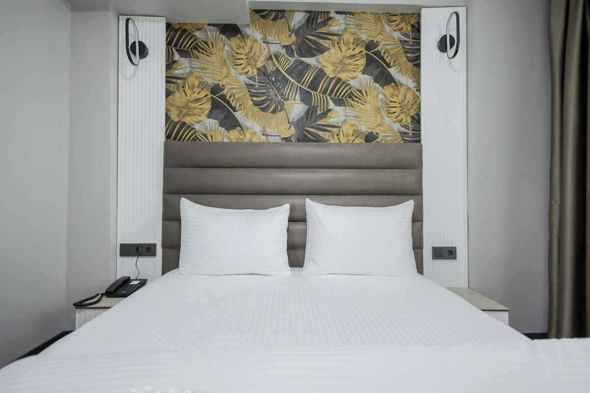 Habitación de hotel con cama, teléfono y pared decorada con un diseño de hojas.