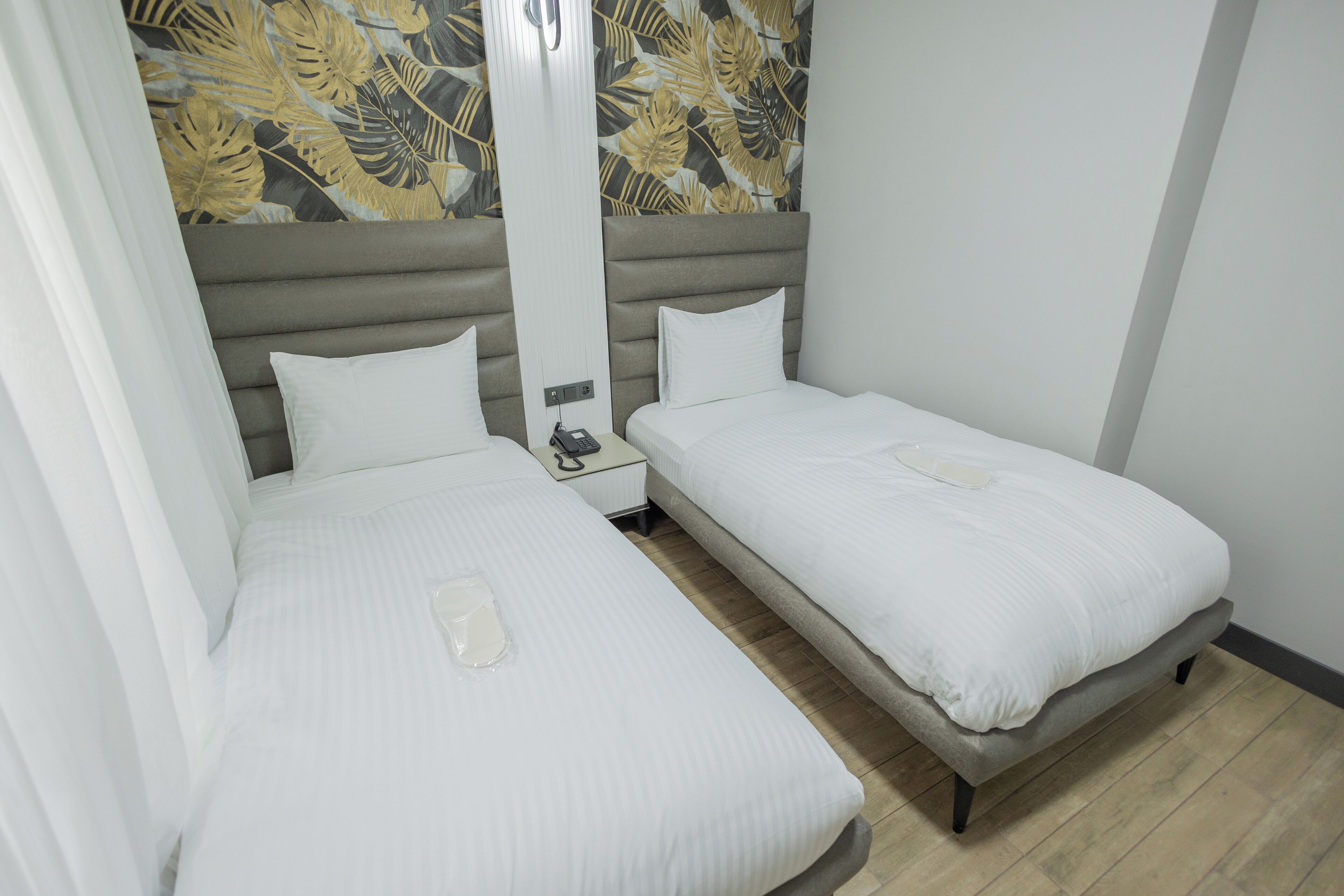Habitación de hotel con dos camas individuales, una mesita de noche con teléfono y una pared con estampado de hojas tropicales.