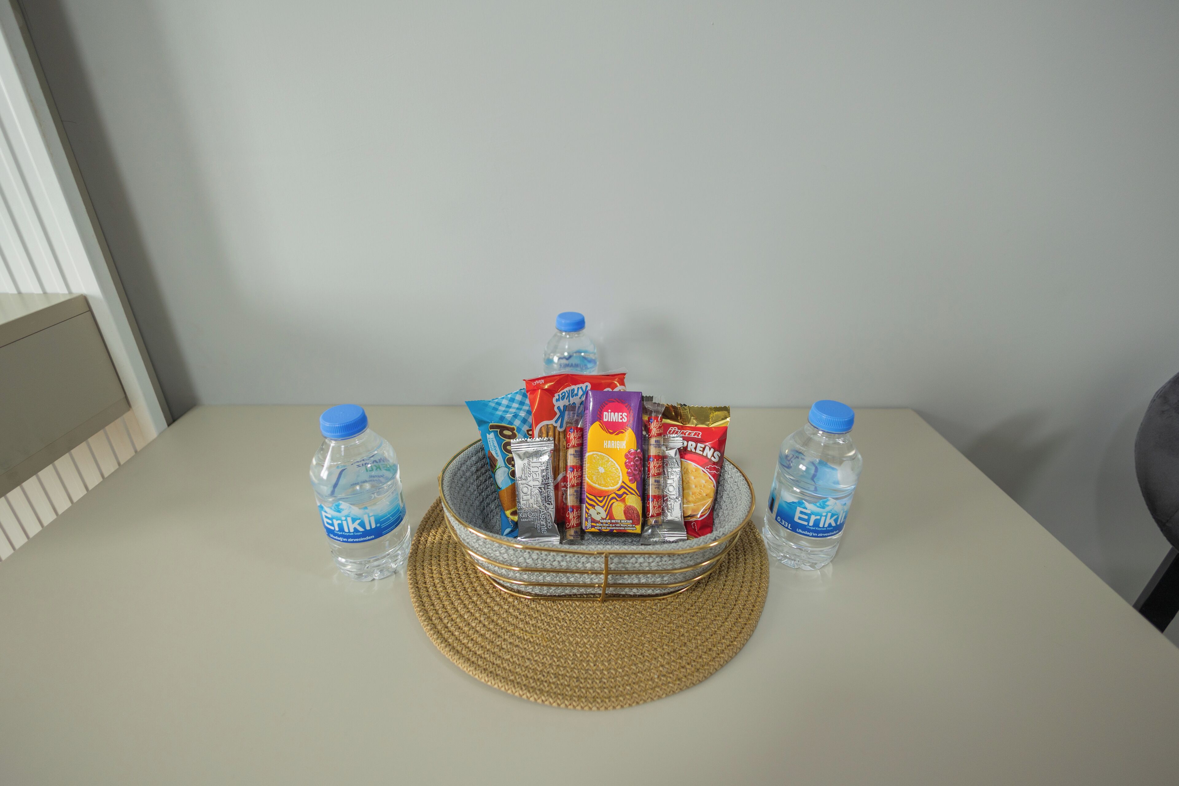 A table with a woven placemat, a basket containing snacks and a water bottle, and two additional water bottles on either side.