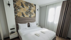 Habitación de hotel con una cama grande, una mesita de noche con teléfono y una pared decorada con un diseño de hojas.