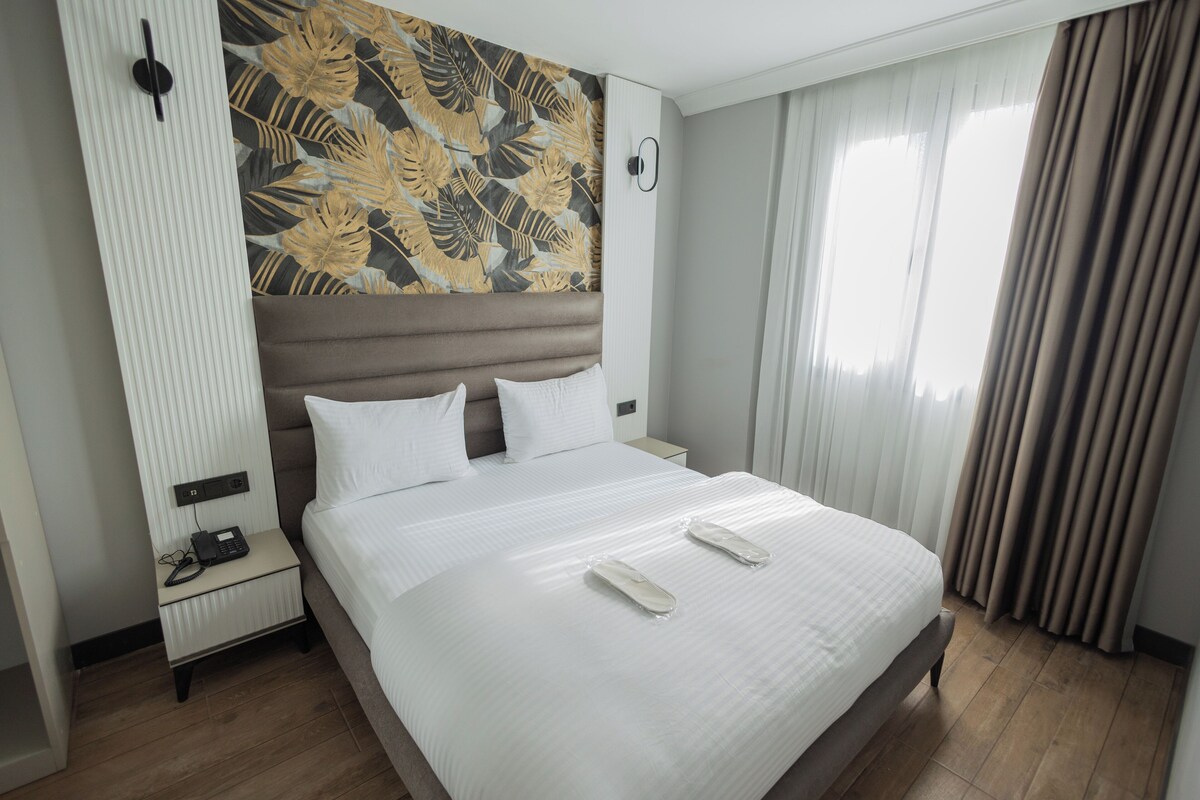 Habitación de hotel con una cama grande, una mesita de noche con teléfono y una pared decorada con un diseño de hojas.