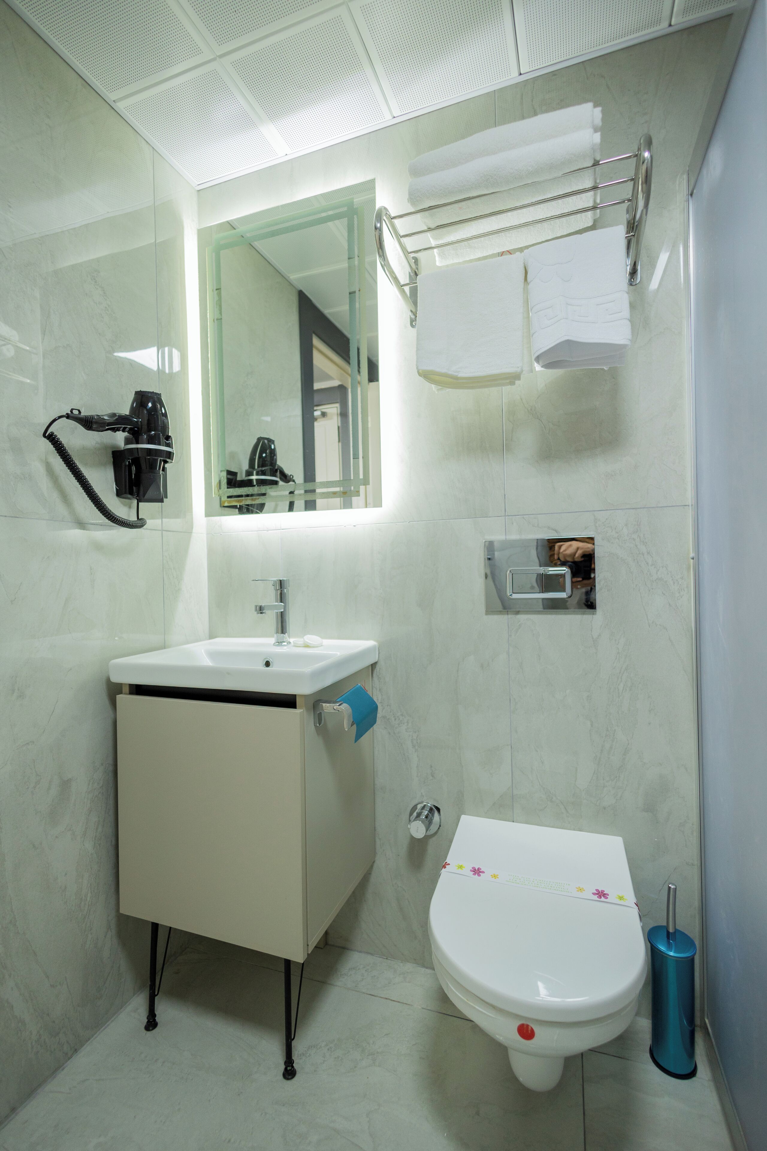 Un baño con lavamanos blanco, un espejo, toallero y un inodoro.
