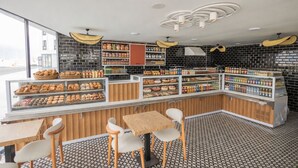 Una panadería con una variedad de productos horneados expuestos en vitrinas y estantes, mesas y sillas de madera, y un piso con diseño.