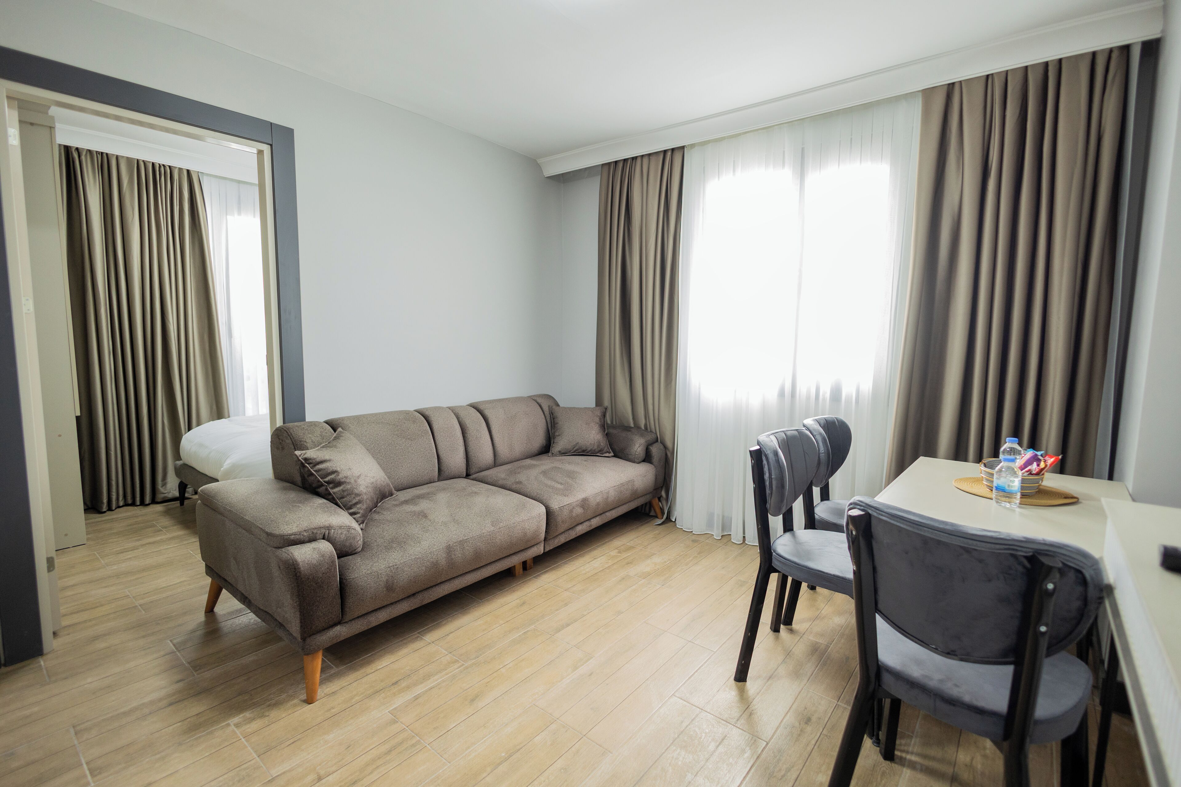 A modern hotel room with a sofa, a dining table with chairs, and a bed.