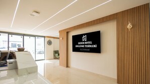 Un moderno área de recepción de hotel con un panel de visualización digital, un mostrador de recepción y un amplio ventanal con vistas al exterior.