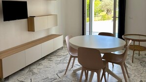 Uma sala de jantar moderna com uma mesa redonda, cadeiras, uma TV fixada na parede, estantes embutidas e um lustre.