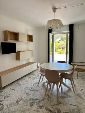 Ein moderner Essbereich mit einem runden Tisch, Stühlen, einer wandmontierten TV, eingebauten Regalen und einer Deckenleuchte.