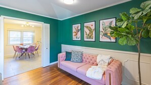 Un salon chaleureux avec un canapé rose, un coin repas avec une table et des chaises, et un couloir menant à une autre pièce.