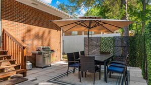 An outdoor patio with a grill, dining table, chairs, and a patterned fence. - Butterfly Bungalow is a 4BR/2BA home with outdoor terrace and grill (Columbus)